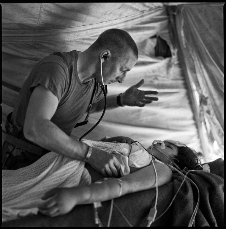 Captain Moore recovers a pregnant Iraqi Shia woman from surgery.  She had been shot through the abdomen by Iraqi Sunni forces.  I did not see it at the time, but the light reflecting off the desert sand though the elevated sides of the tent created a presence, a power behind Captain Moore, guiding and working through him.  In my mind, the photograph captures four souls because, at this point at least, the baby was still viable.
To see the entire portfolio please go to https://www.934fst.com