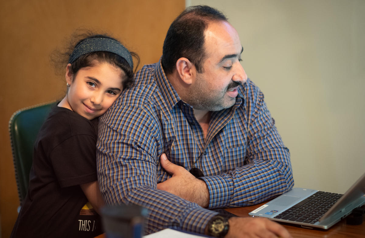 Deema Swidan holds her father, Salwan Swidan, while he studies for his medical boards.  Both are refugees from Iraq where Swidan was a cardiologist practicing in Baghdad.  He has been studying for years to take the U.S. board examination which will qualify him to re-enter an American residency training program to train all over again.  This photo was made toward the end of a grueling 3-hour study session, held on a Sunday, with other physicians.  

Deema and her brother had been studying in another room while I photographed the study session.  She left her brother, walked up behind her father and gave him this hug, as if to both acknowledge and thank him for his hard work, and perhaps to tell him it was time to go home.